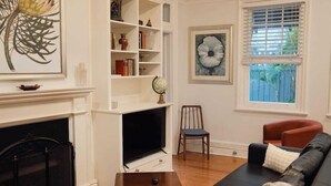 A living room with a fireplace, a black sofa, a red armchair, a bookshelf, and a large window with blinds. - Manly Designer Studios (Sydney)