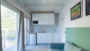 A modern kitchen with white cabinets, a microwave, and a small refrigerator. There is a balcony with a view of greenery. - Manly Designer Studios (Sydney)