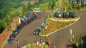 Un parking où sont garées plusieurs voitures et un autobus, entouré de verdure et de bâtiments résidentiels.