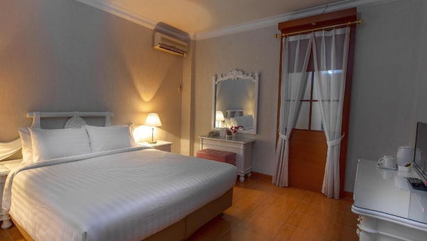 Une chambre d’hôtel avec un grand lit, des tables de chevet avec des lampes, une coiffeuse avec un miroir, un bureau avec une chaise et une fenêtre avec des rideaux.