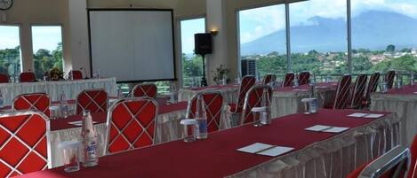 A conference room with multiple tables, chairs, and a large screen.