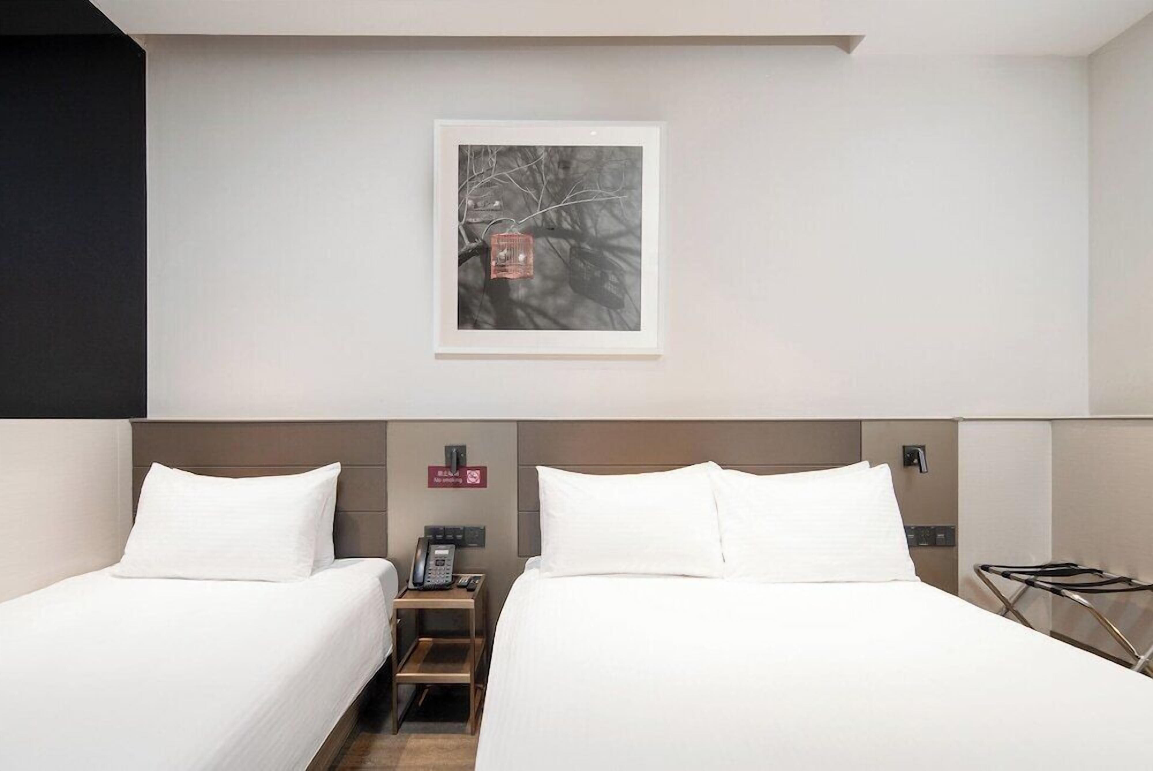 A hotel room with two beds, a nightstand with a phone, and a framed picture on the wall.