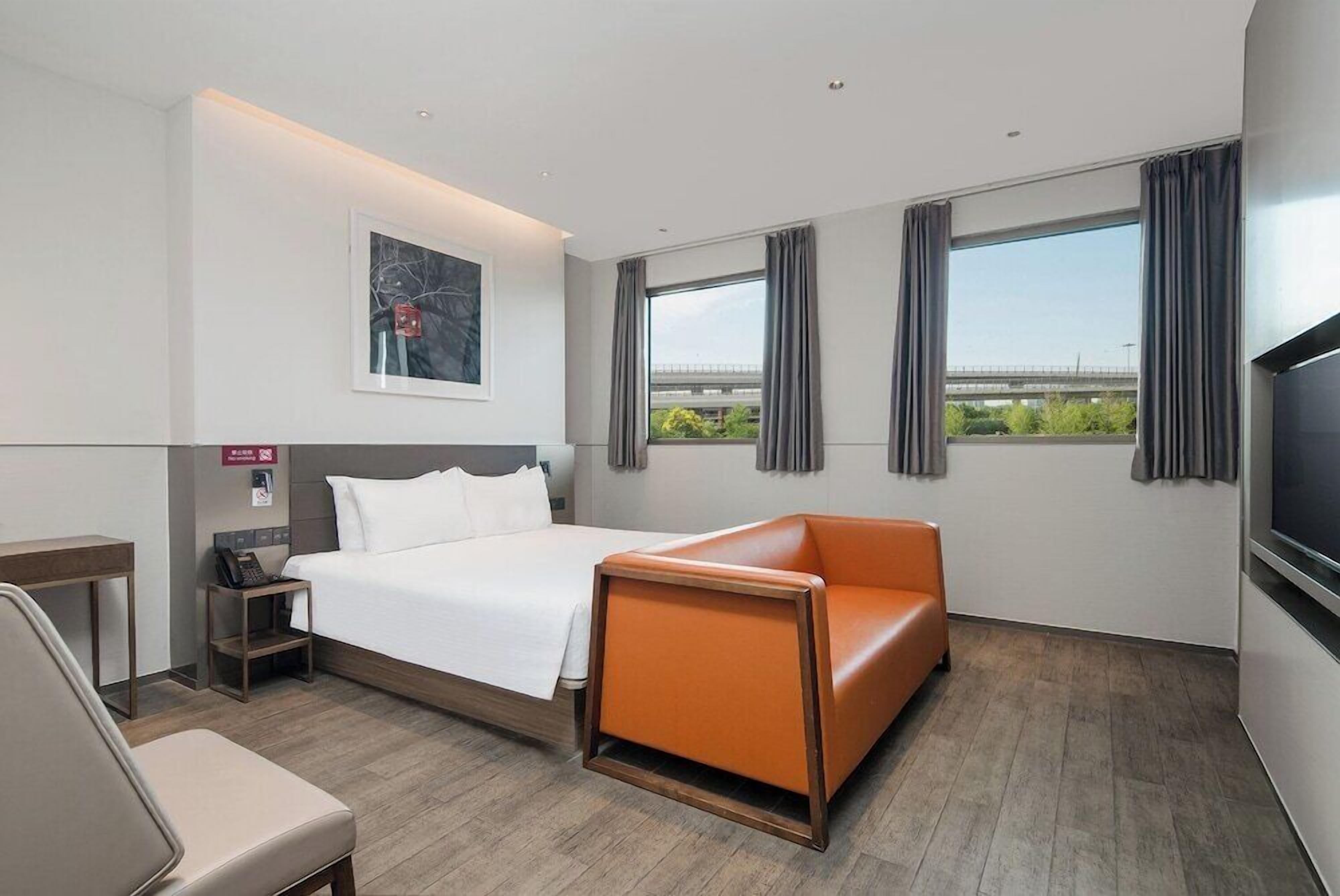 Ein modernes Hotelzimmer mit Bett, einer Couch, einem Schreibtisch und einem großen Fenster mit Vorhängen.