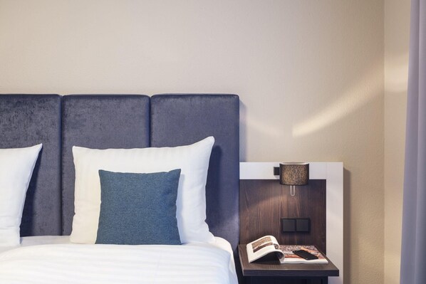 A neatly made bed with white and blue bedding, a wooden nightstand with a lamp, and a book. - Select Hotel Elmshorn (Elmshorn)