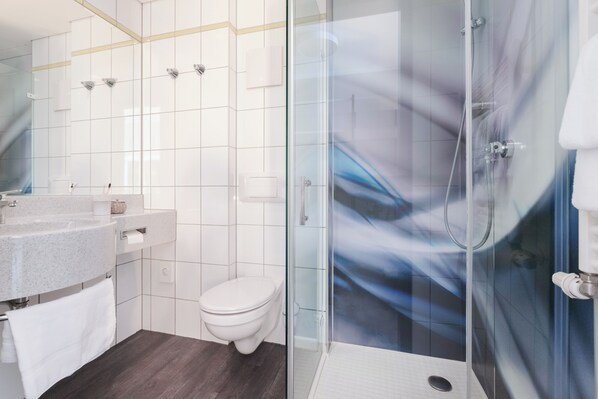 A modern bathroom with a glass shower enclosure, a white toilet, and a granite sink with a towel. - Select Hotel Elmshorn (Elmshorn)