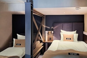 A hotel room with two beds, a nightstand, a lamp, and a headboard.