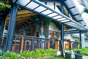 An indoor/outdoor cafe with a covered seating area, a large tree, and a view of the building's interior. - Hotel Ariandri (Cisarua)