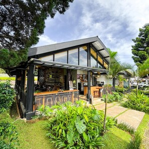 A modern bar with a glass enclosure, outdoor seating, and lush greenery. - Hotel Ariandri (Cisarua)