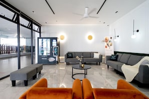 A modern interior with a sofa, ottoman, and coffee table, a vending machine, and a wall with a poster. - Windmill Premier Suites Genting Highlands (Genting Highlands)