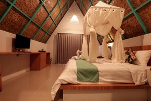 A bedroom with a bed, a TV, a desk, and a thatched ceiling.