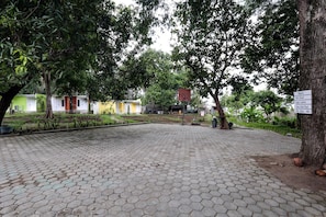 A paved courtyard with hexagonal tiles, surrounded by trees and buildings with signage indicating directions to various locations. - Makarma Resort Lombok (Senggigi)