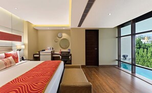 Habitació d'hotel moderna amb un llit gran, escriptori, petita cuina i una finestra amplia amb vistes a vegetació.
