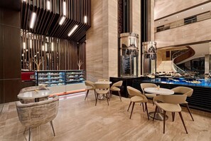 A modern lobby with a central staircase, a seating area with round tables and chairs, and a display of shoes. - Fortune Park Vellore (Katpadi)