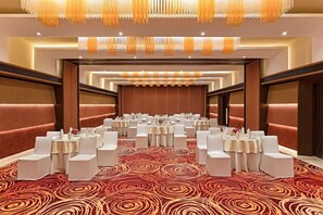 Un salón de conferencias con mesas redondas, sillas blancas y una alfombra estampada.