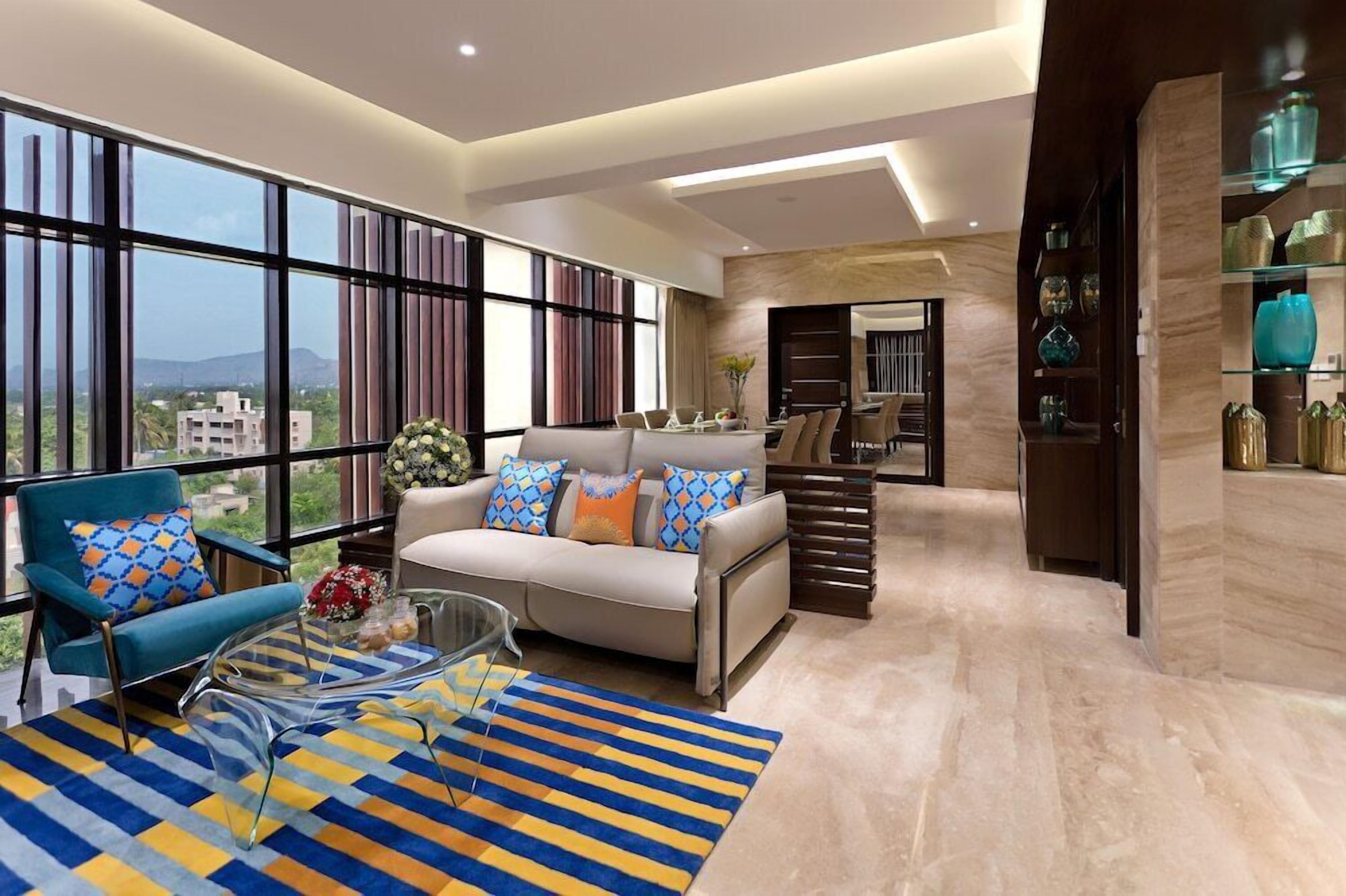 A modern living room with a sofa, armchair, and coffee table, large windows, and a view of buildings.