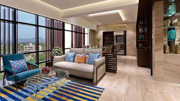 A modern living room with a sofa, armchair, and coffee table, large windows, and a view of buildings.