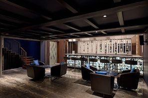 Zona de bar moderna con suelo de mármol, taburetes negros y una vitrina para vinos.