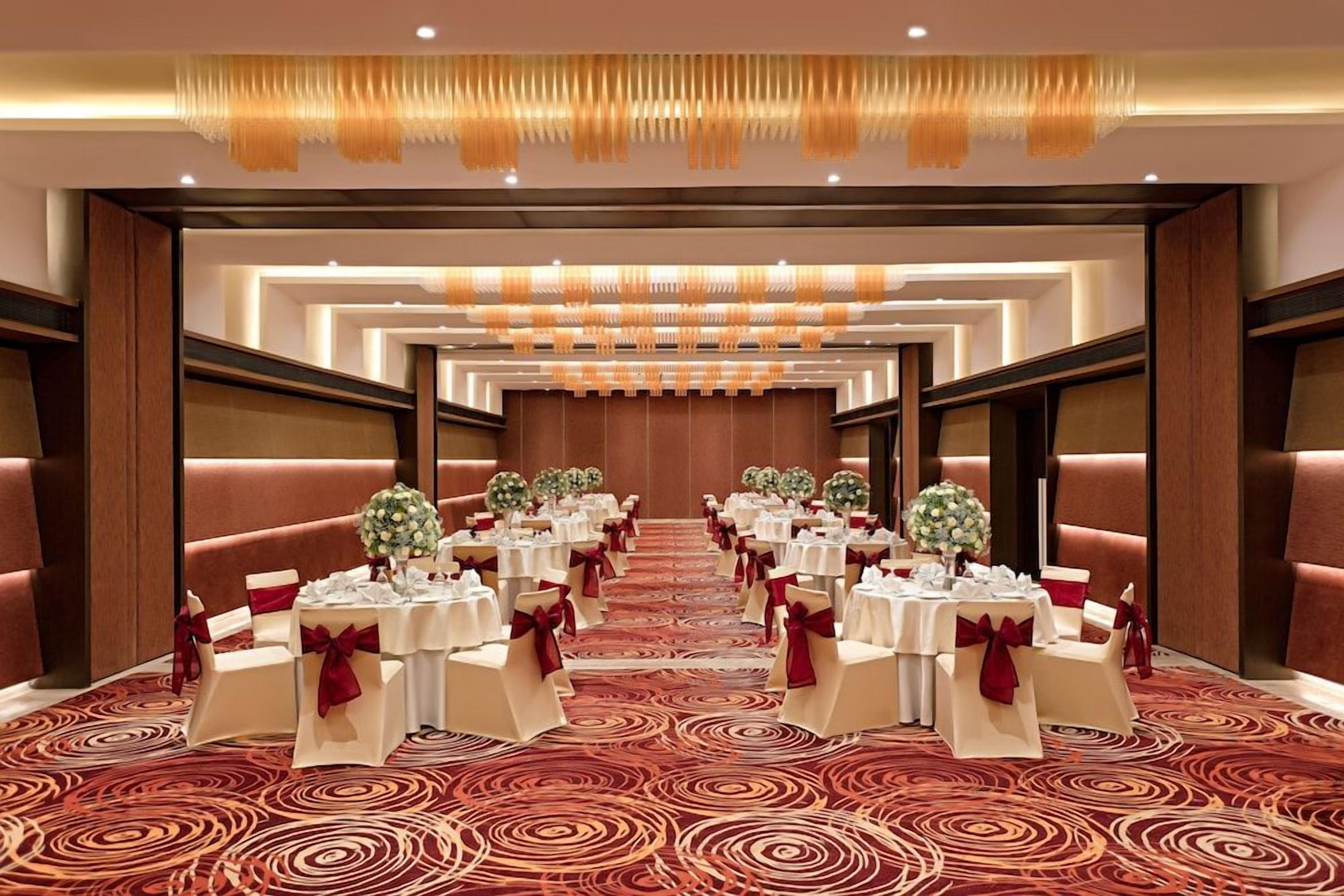 A banquet hall with round tables, red and white chairs, and a red carpet.