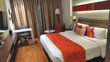 A hotel room with a bed, a desk, a chair, a small table, and a lamp.