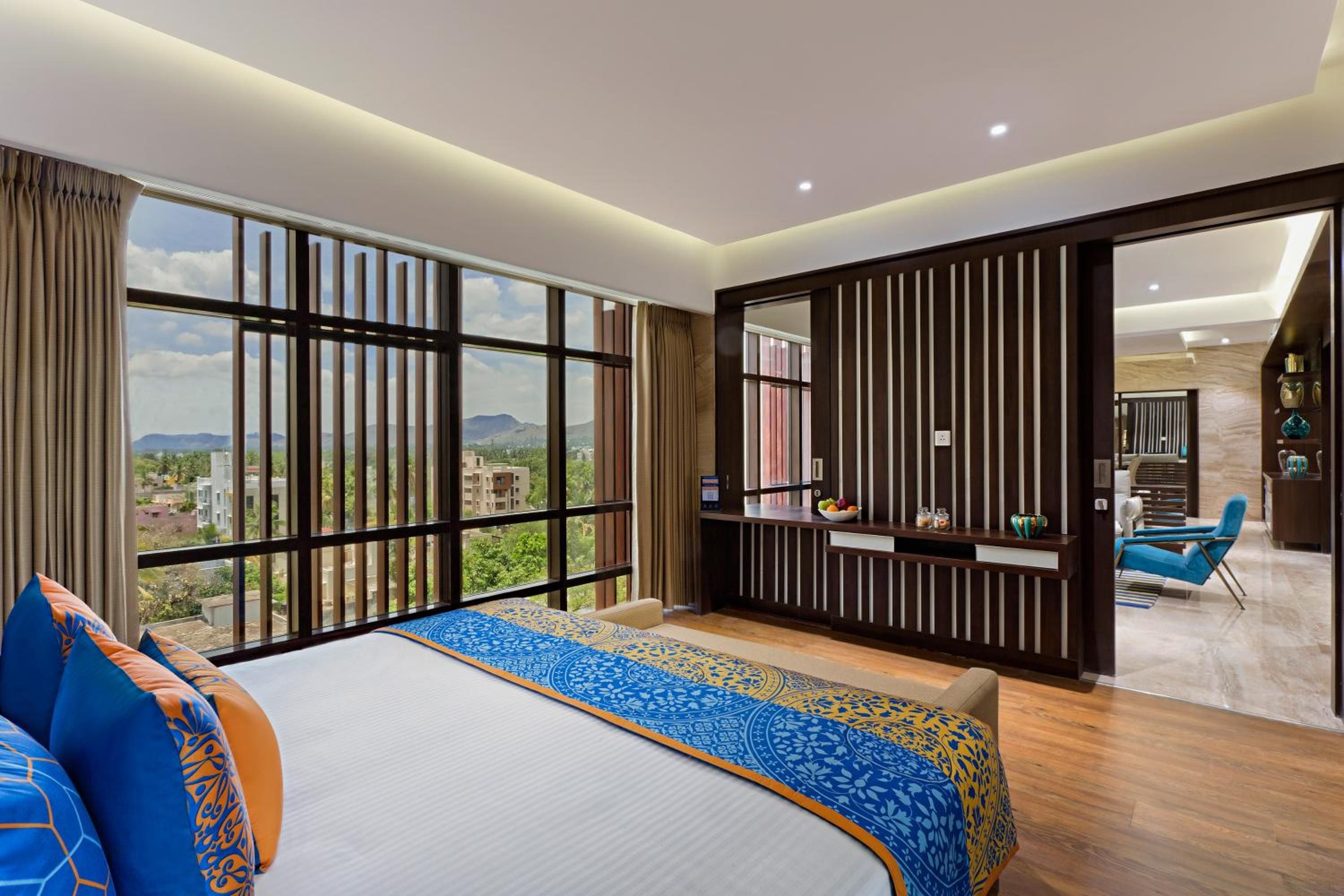 A hotel room with a large bed, a view of the city, and a balcony with a seating area.