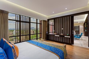 A hotel room with a large bed, a view of the city, and a balcony with a seating area. - Fortune Park Vellore (Katpadi)