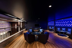 A modern lounge area with a central round table surrounded by black leather sofas, wooden flooring, and blue ambient lighting. - Fortune Park Vellore (Katpadi)