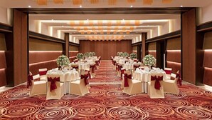 A banquet hall with round tables, red and white chairs, and a red carpet.