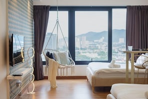 Una habitación de hotel moderna con un ventanal grande, un sillón colgante, una cama, un televisor y una mesita.