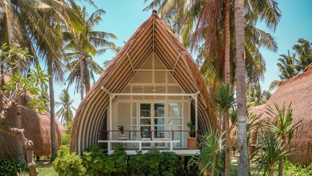 Ein Bungalow mit Strohdach und Balkon, umgeben von tropischer Vegetation.