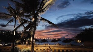 Blick auf einen Pool im Abenddämmerung mit Palmen, Sonnenuntergang und Strandstühlen.