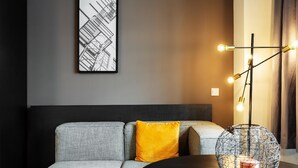 Un salon moderne avec un canapé gris, un coussin jaune, une table ronde et un luminaire sphérique original.