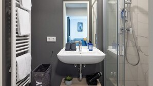 Une salle de bain moderne avec un lavabo blanc, une cabine de douche en verre et un porte-serviettes avec des serviettes pliées.
