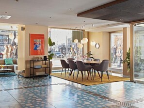 A modern hotel lobby with a dining area, large windows, and a view of the street. - Joyn Cologne (Cologne)