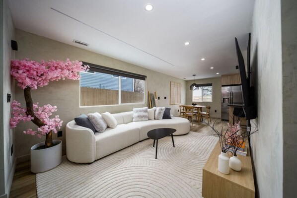 A modern living room with a white sectional sofa, a black coffee table, and a large window with a view of a wooden deck.