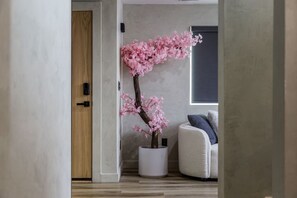A room with a wooden door, a white vase with pink flowers, and a grey sofa.