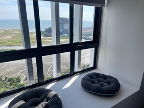 A room with a large window overlooking a coastal landscape, two black cushions on a white ledge, and a white wall. - Imperio Residences by Lets Stay (Malacca City)