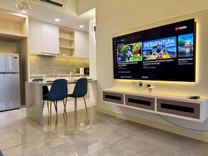A modern kitchen with a built-in TV displaying a YouTube channel, a refrigerator, and a dining area with two chairs. - Imperio Residences by Lets Stay (Malacca City)