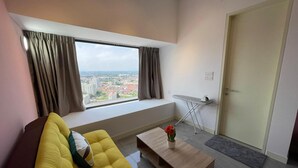 Una sala moderna con un sofá amarillo, una mesita de centro de madera, vista a un paisaje urbano a través de un ventanal grande y una puerta a la derecha.