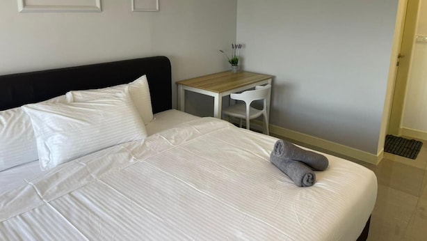 Una cama bien hecha con ropa blanca, una mesita de madera con una silla, y un florero con flores en la pared.