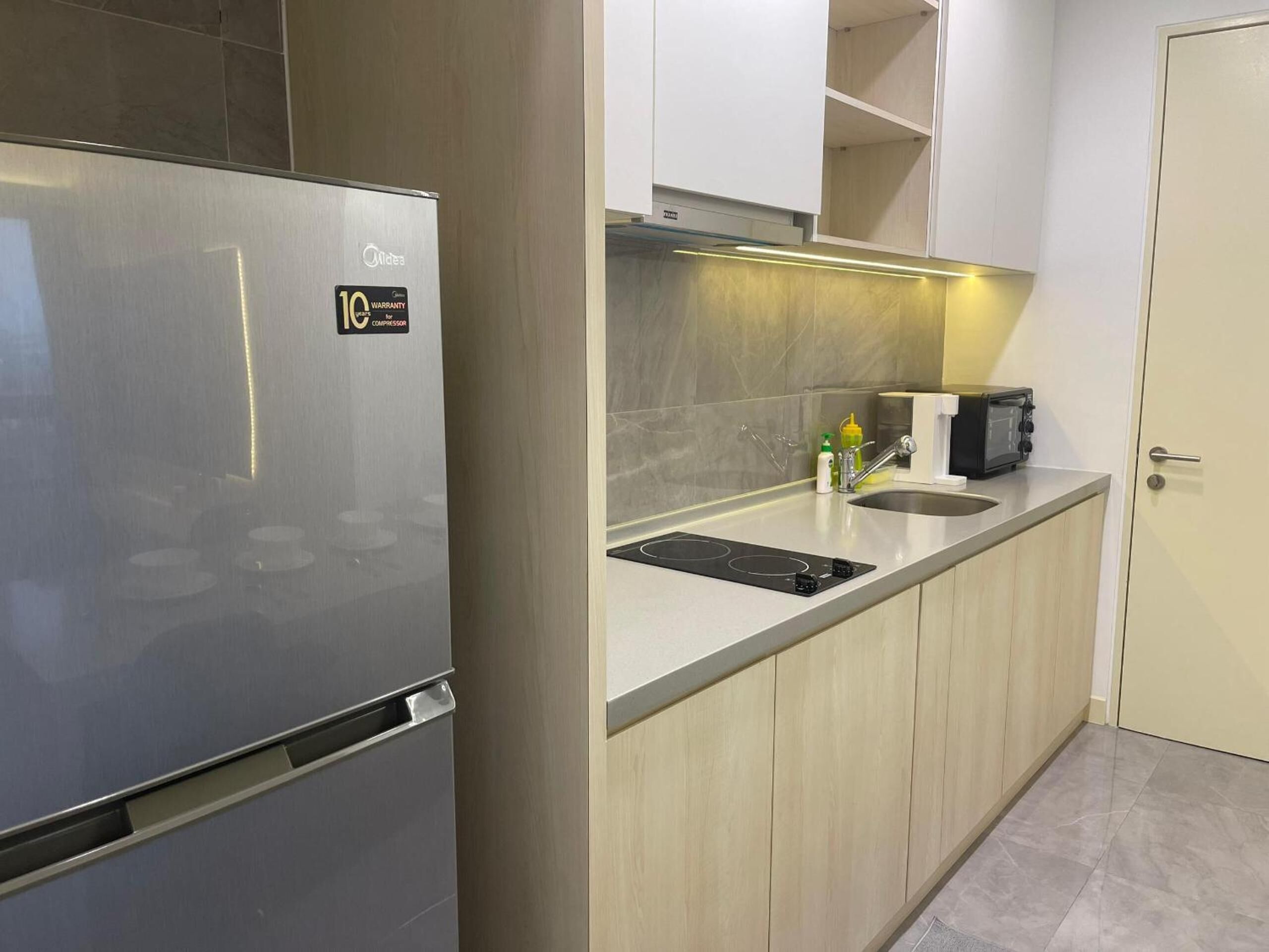 A compact kitchen with a stainless steel refrigerator, a built-in oven, a sink, and a toaster.