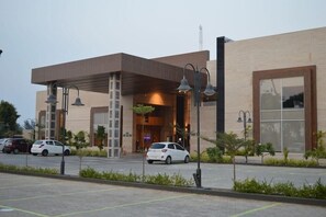 A modern building with a covered entrance, a parking lot, and a few cars parked in front. - Welcomhotel by ITC Hotels, Kences Palm Beach (Tirukalukundram)