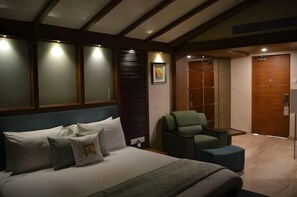 Une chambre d’hôtel avec un lit, un fauteuil vert, une armoire en bois et un tableau encadré au mur.