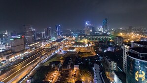 Een verlicht stadsbeeld 's nachts, met gebouwen, een snelweg en een parkeerplaats.