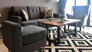 Ein modernes Wohnzimmer mit grauem Sofa, einem passenden Sessel, einem Holztisch und einem gemusterten Teppich.