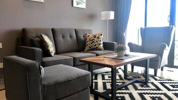 A modern living room with a grey sofa, a matching armchair, a wooden coffee table, and a patterned rug.