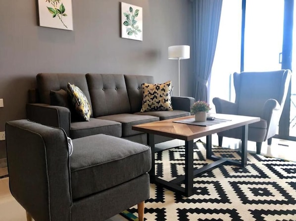 Un salon moderne avec un canapé gris, un fauteuil assorti, une table basse en bois et un tapis à motifs.