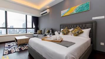 A modern hotel room with a large bed, a city view, a gray sofa, and a painting on the wall.
