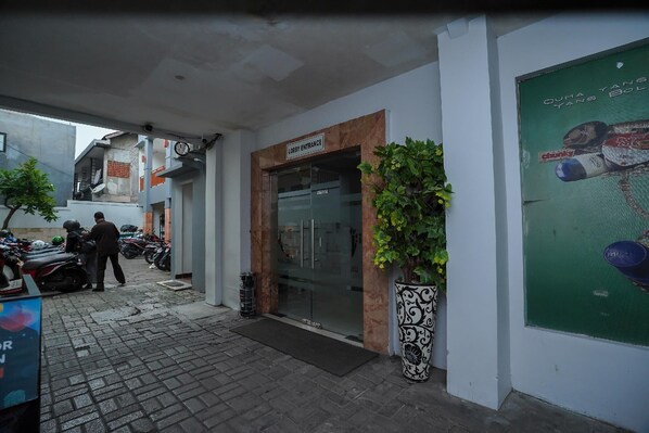 Entrada de recepción con puerta de vidrio, una planta en maceta y un cartel que indica la zona de recepción.