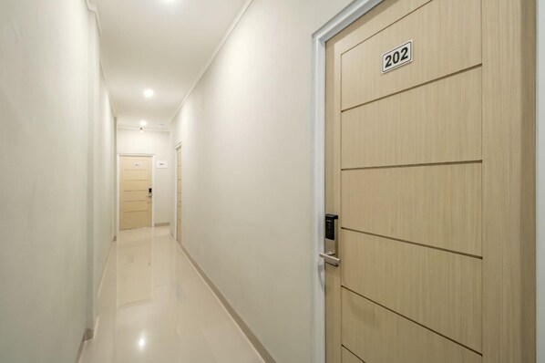 Um corredor com uma porta de madeira com a inscrição '202' e outra porta ao longe com a inscrição '214'.