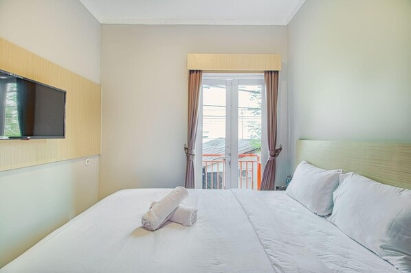 Habitación de hotel con cama, televisor montado en la pared y vista al balcón.